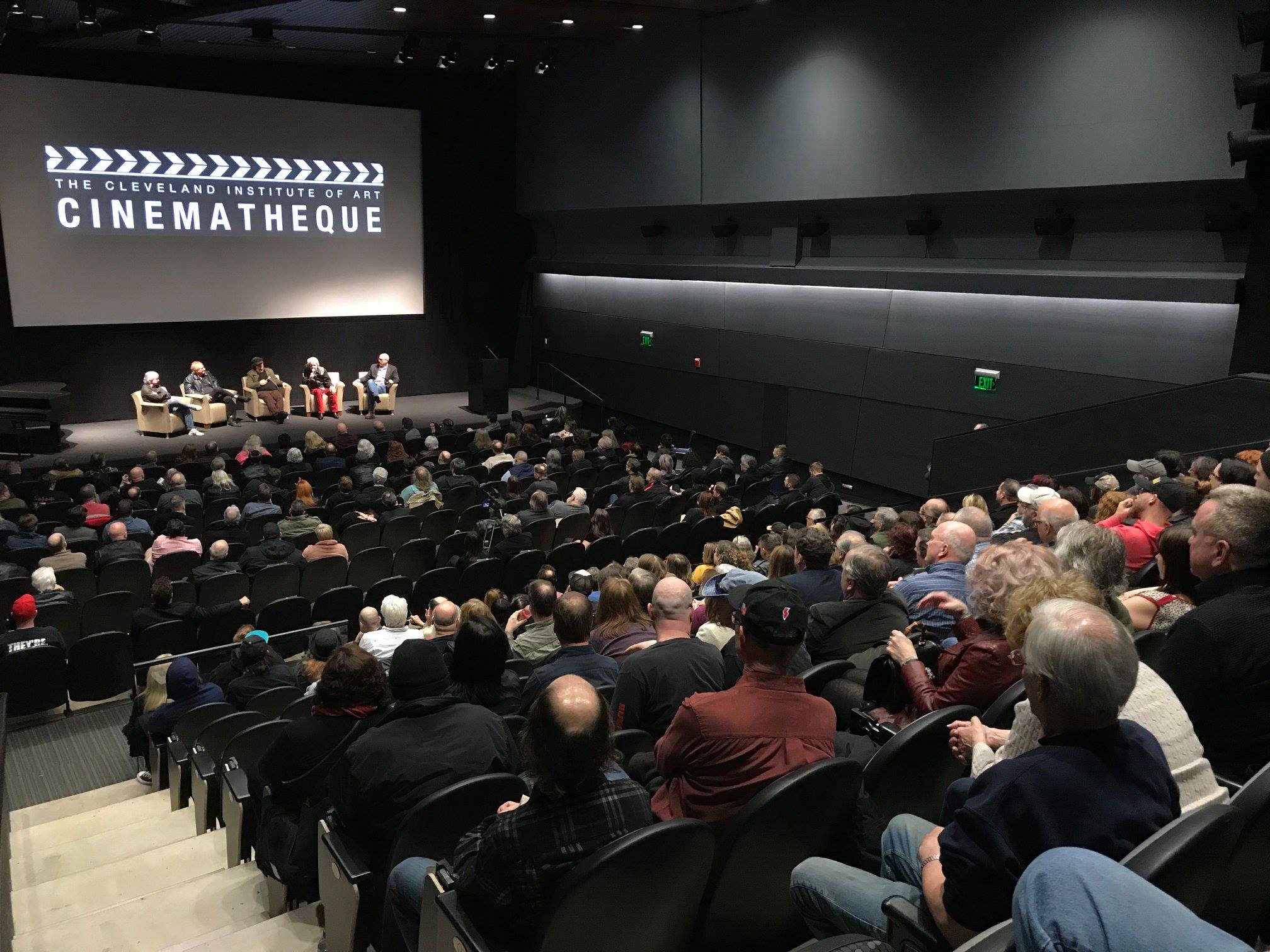 A top view in the Peter B. Lewis. The crowd is mostly full and there is a panel on the stage talking before a film premiere.